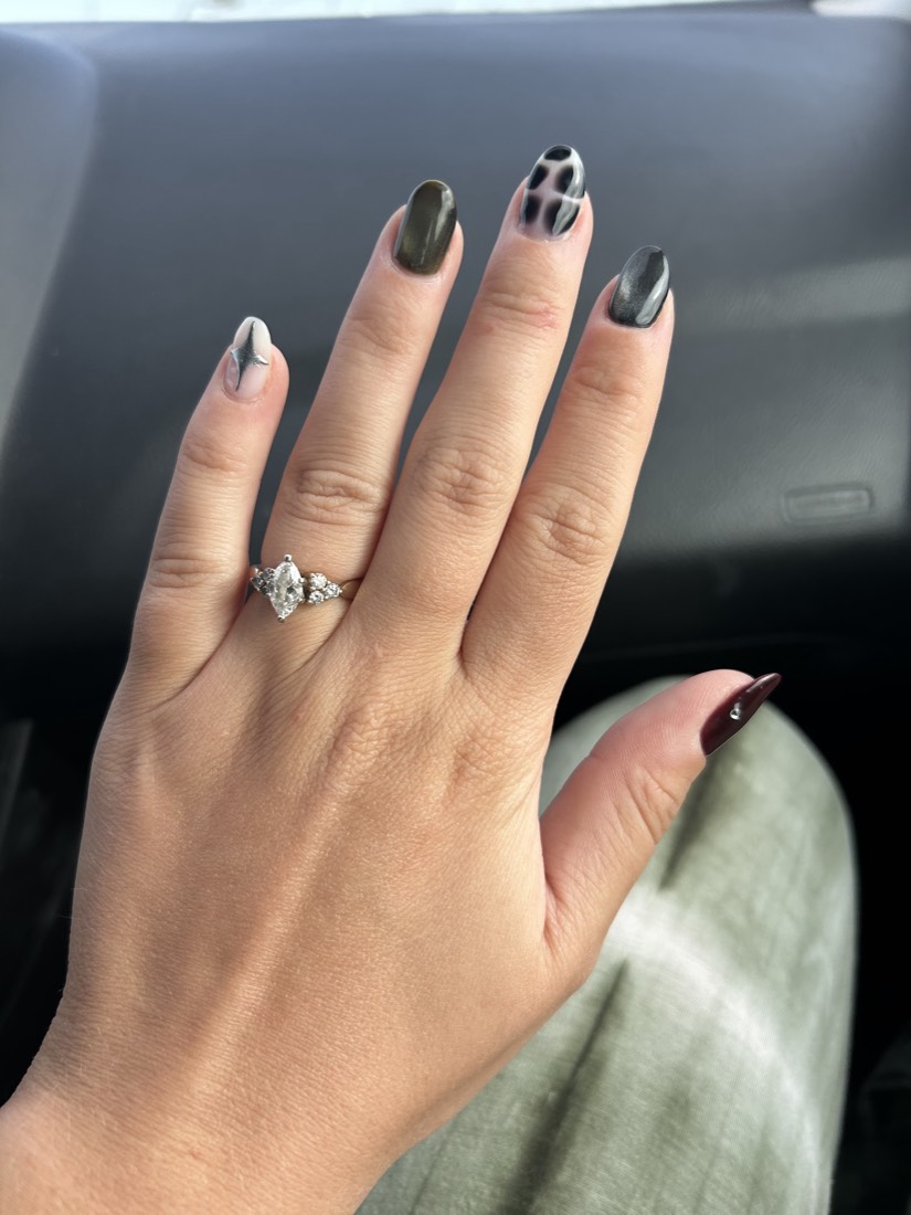 A hand with olive-green, chrome and black-and-white cheetah-print nail art and a diamond ring