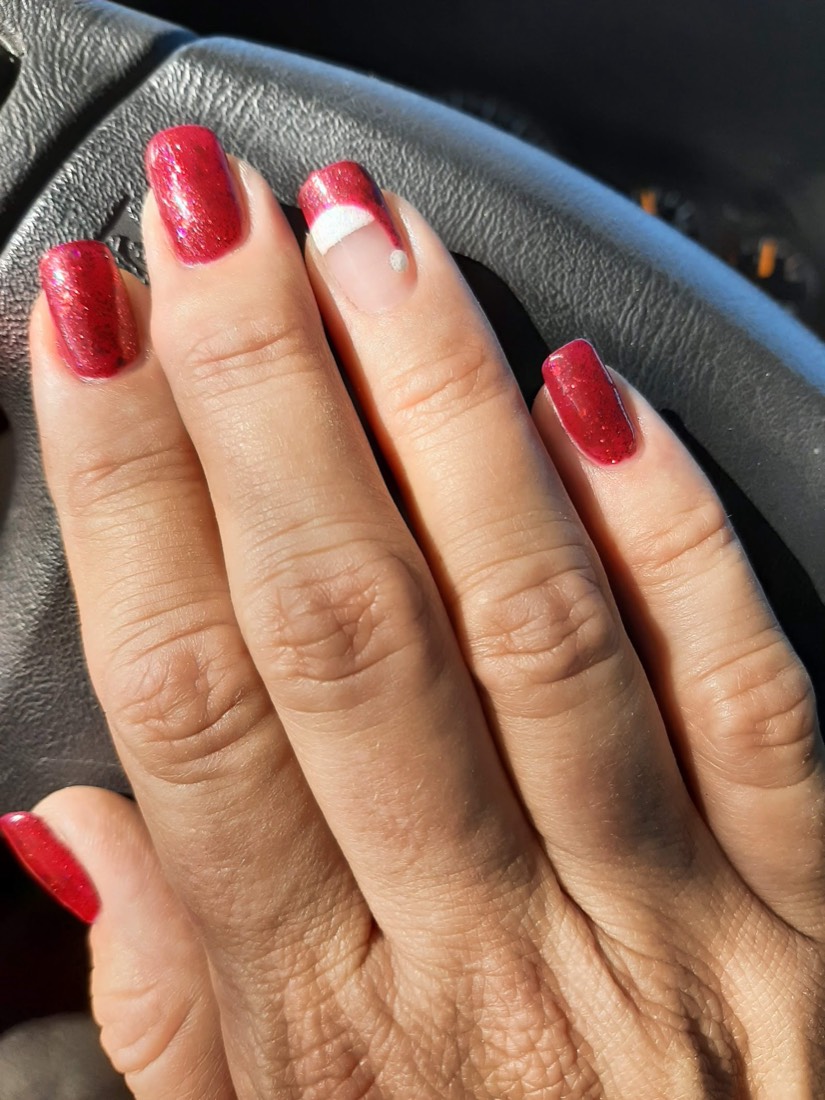 A hand with deep red glitter gel nails and one white accent nail