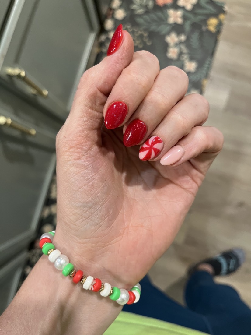 A hand with glossy red nails and one nail hand-painted with a red-and-white peppermint swirl