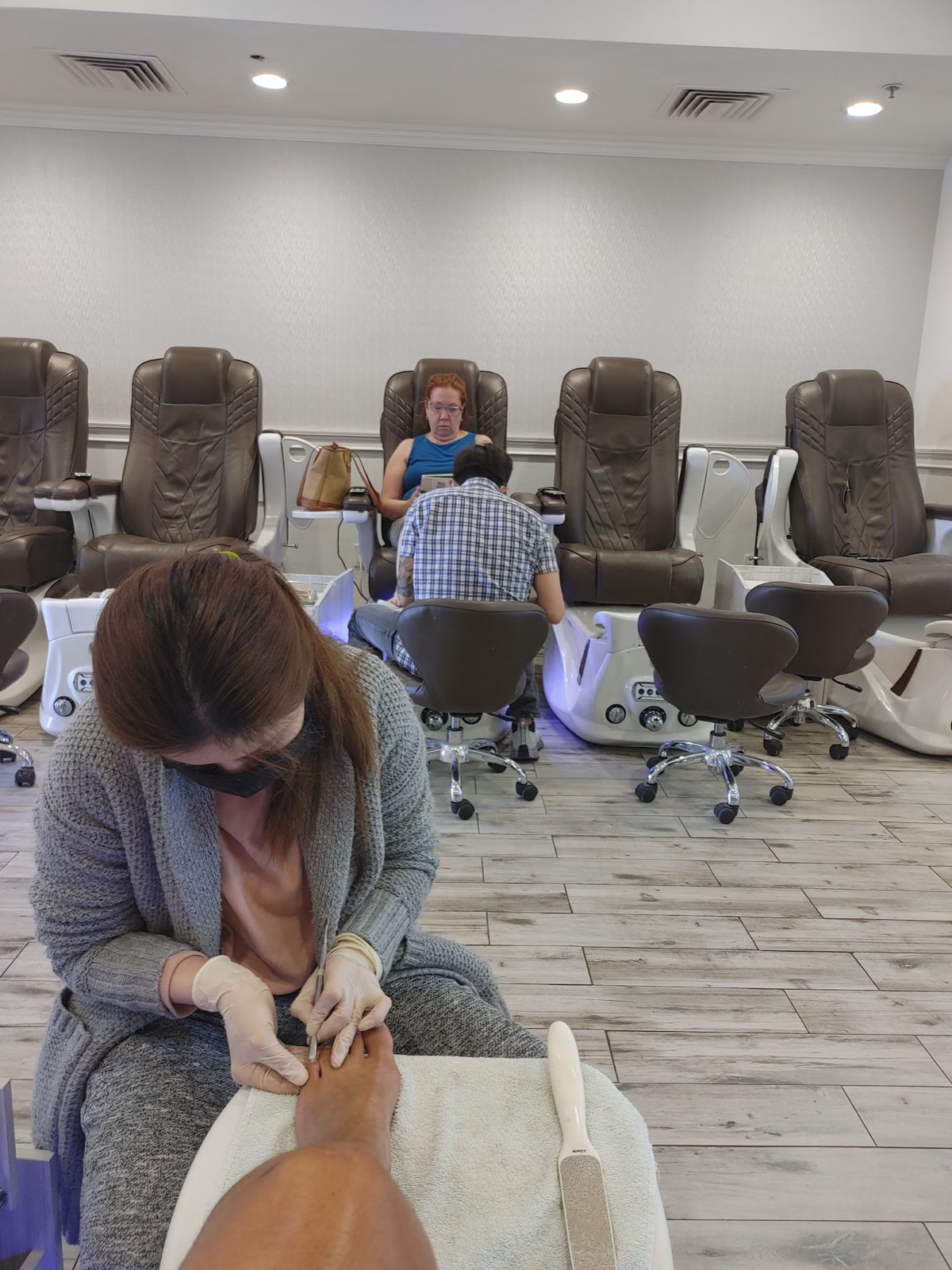 Inside ONE Nail Lounge: a row of cushioned pedicure chairs along a bright wall while a technician works on a client's feet